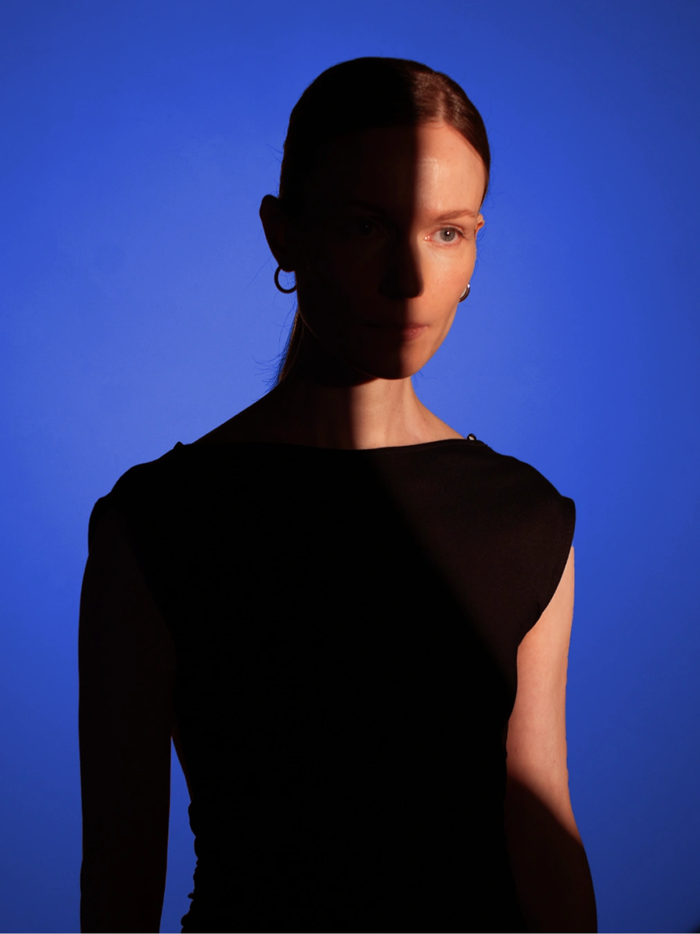 Portrait of a woman in partial shadow with blue backdrop and dramatic lighting.
