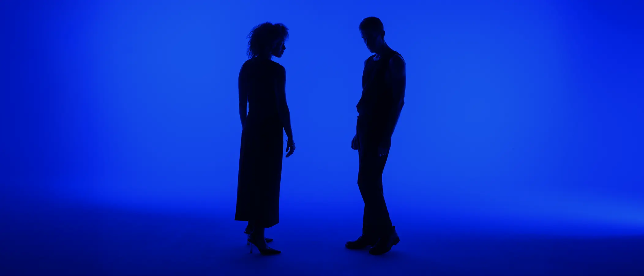 Two silhouettes of people standing and conversing against a vibrant blue gradient background
